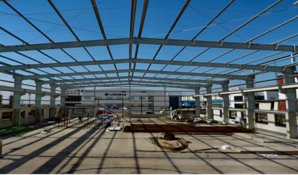 A Large Open Frame Steel Structure Under Construction With Various Building Materials Scattered On The Ground.